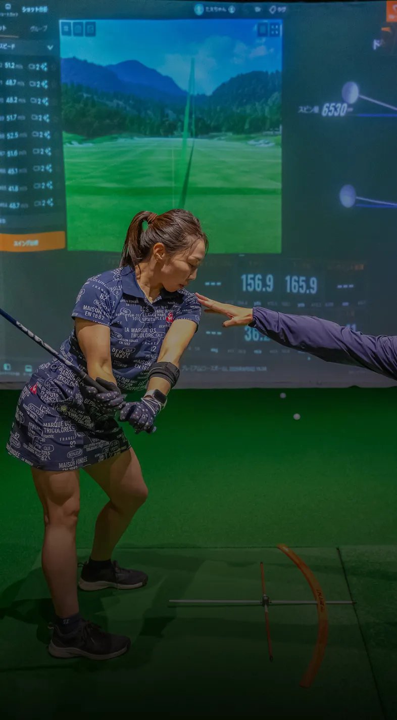 A woman in a golf swing stance receives guidance from an instructor in an indoor golf simulator.