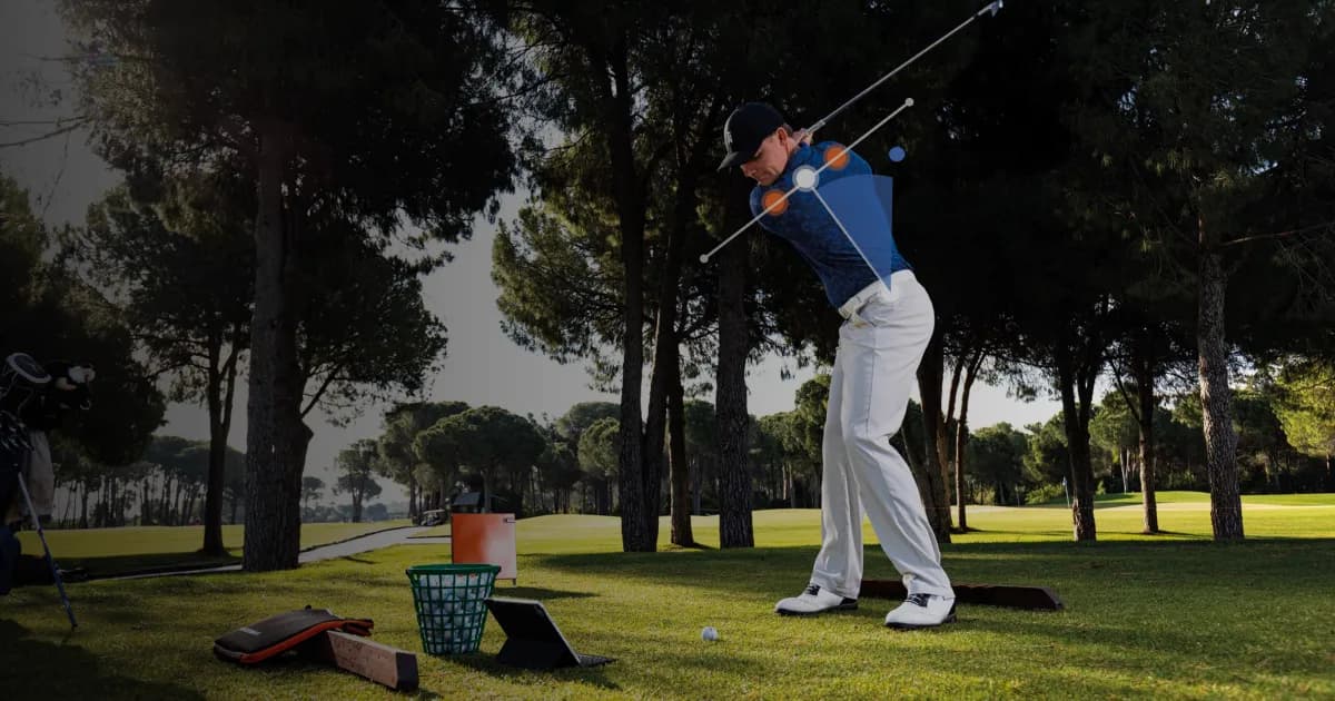 Golfer practicing swing at a driving range, surrounded by trees, with training equipment and basket of balls on the grass.