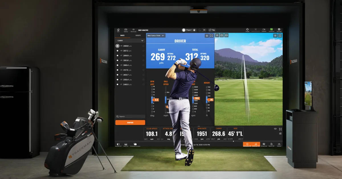A golfer swings indoors using a golf simulator, displaying stats and a virtual course on a large screen. Golf clubs are nearby.