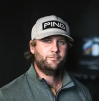 A person wearing a gray cap with "PING" on it and a green zip-up jacket stands against a dark background, looking towards the camera.