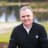 Smiling man in a dark jacket with a golf course background.