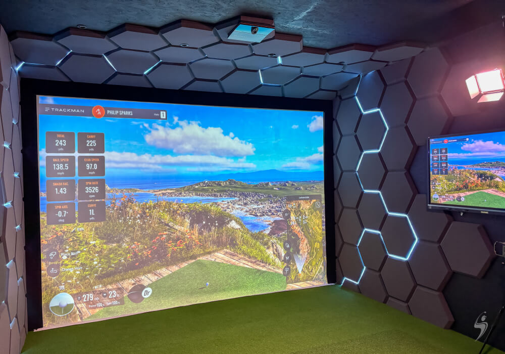 Trackman iO Golf simulator room with a large screen displaying a coastal golf course and a smaller screen showing game stats.