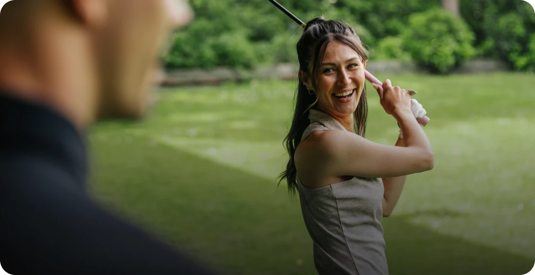 Woman smiling while holding a golf club, standing on a lush green golf course.