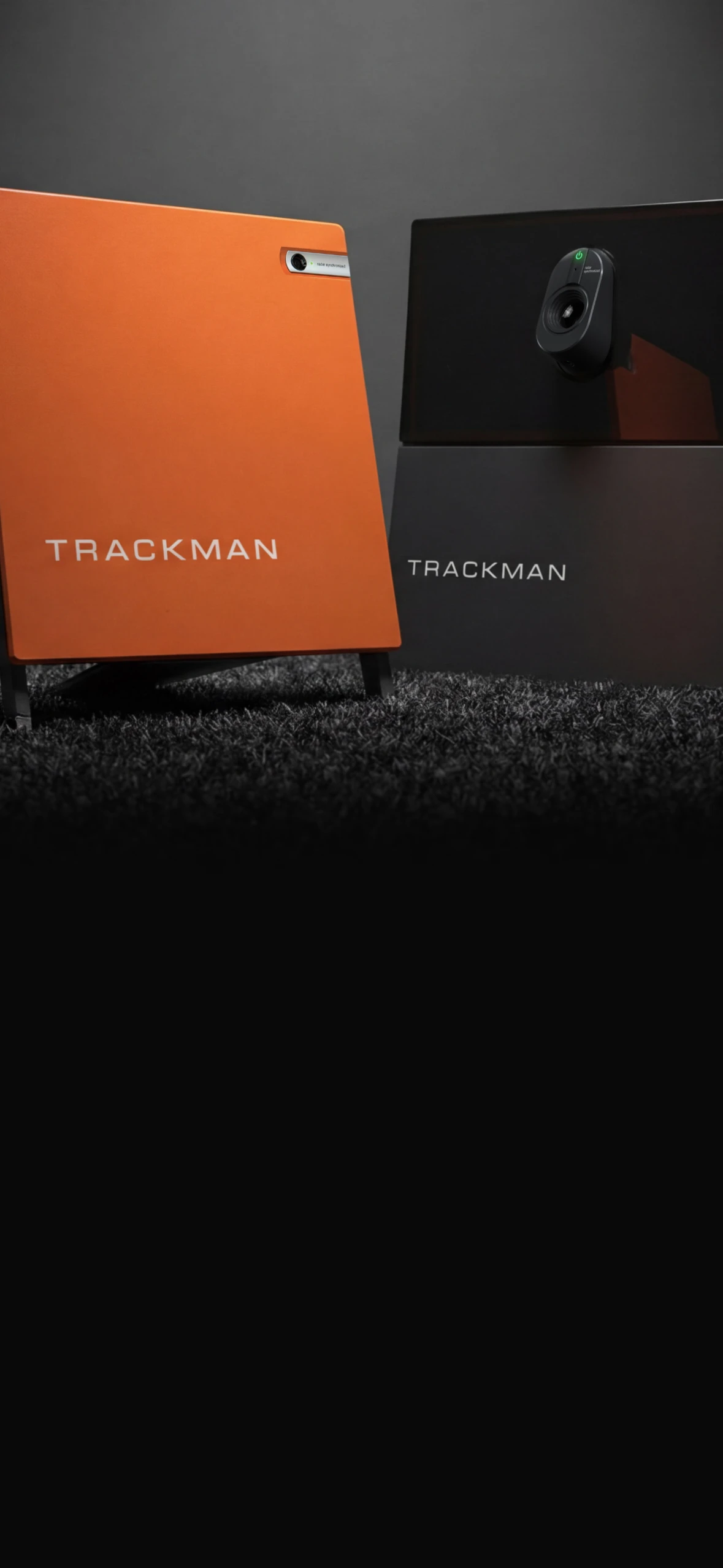Orange and black TrackMan devices on a textured surface, with a camera lens visible on the black unit.
