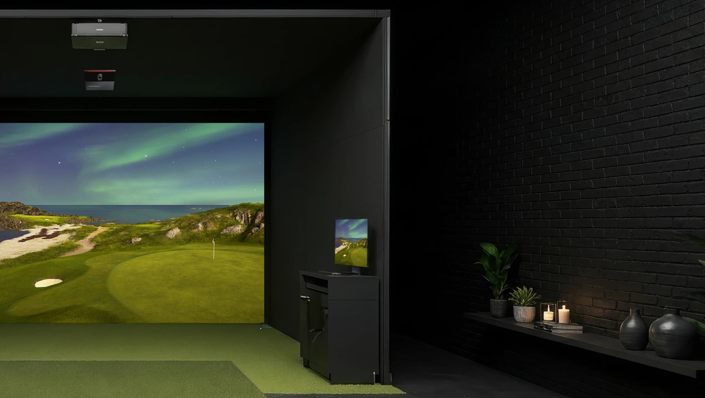 Indoor golf simulator with a green landscape on the screen. Dark room with black brick walls, plants, candles, and small decor items.