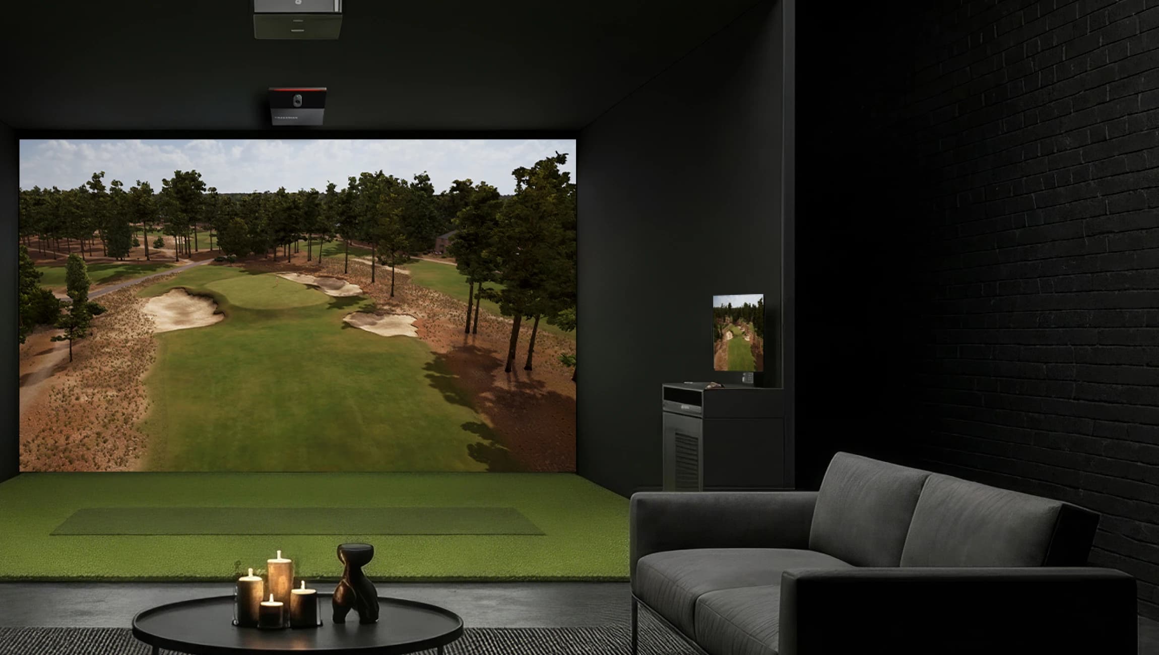 A virtual golf simulator setup in a dark room with a large screen displaying a golf course, a sofa, and a table with candles.