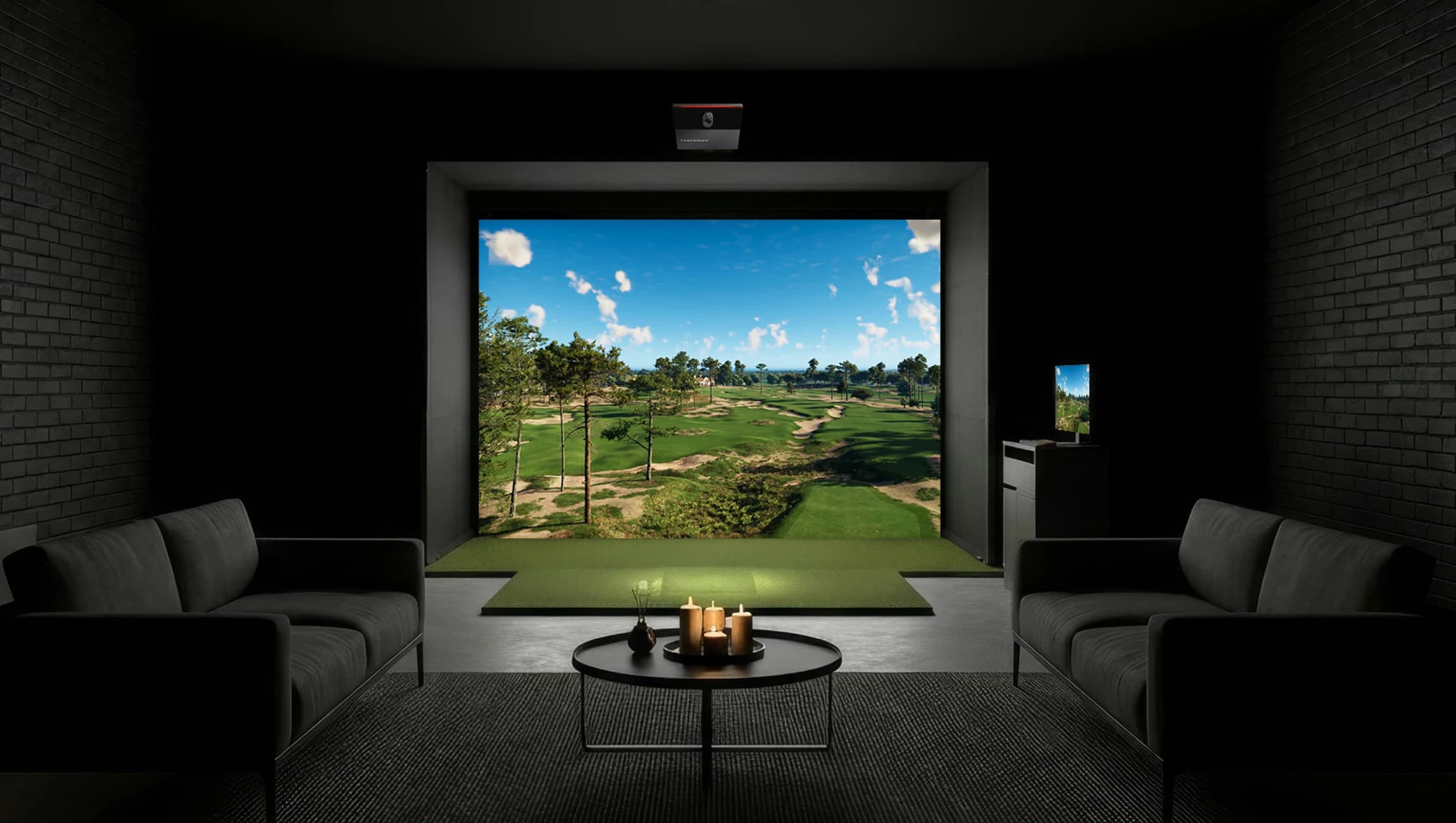 Modern room with golf simulator, sofas, a round table with candles, and a view of a sunny golf course displayed on the screen.