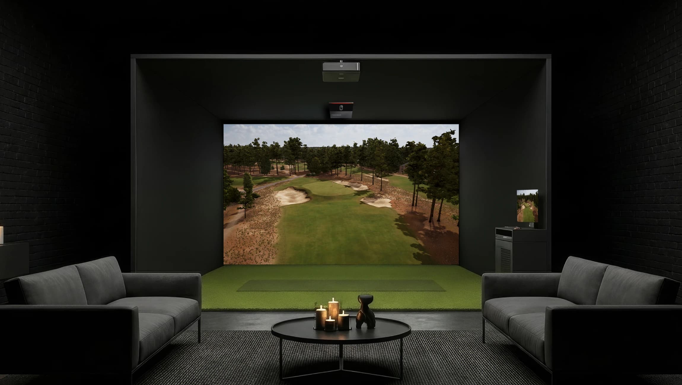 Modern indoor golf simulator room with a large screen displaying a golf course, two gray sofas, and a coffee table with candles.