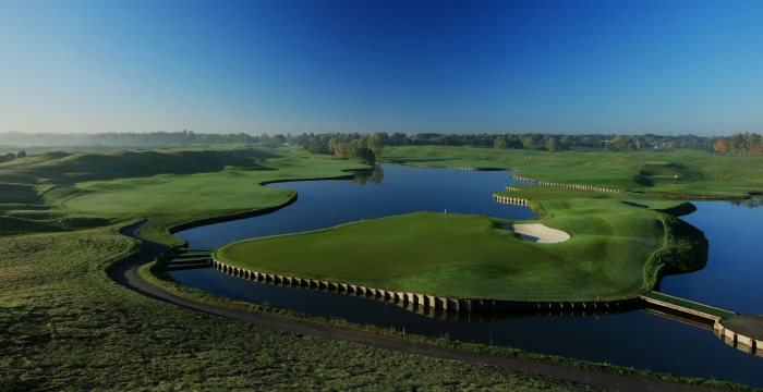 A golf course surrounded by water features and lush greenery under a clear blue sky.