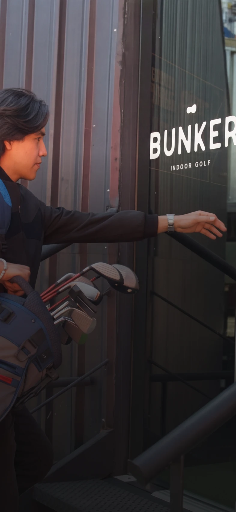 A person carrying a golf bag reaches for a door labeled "Bunker Indoor Golf."