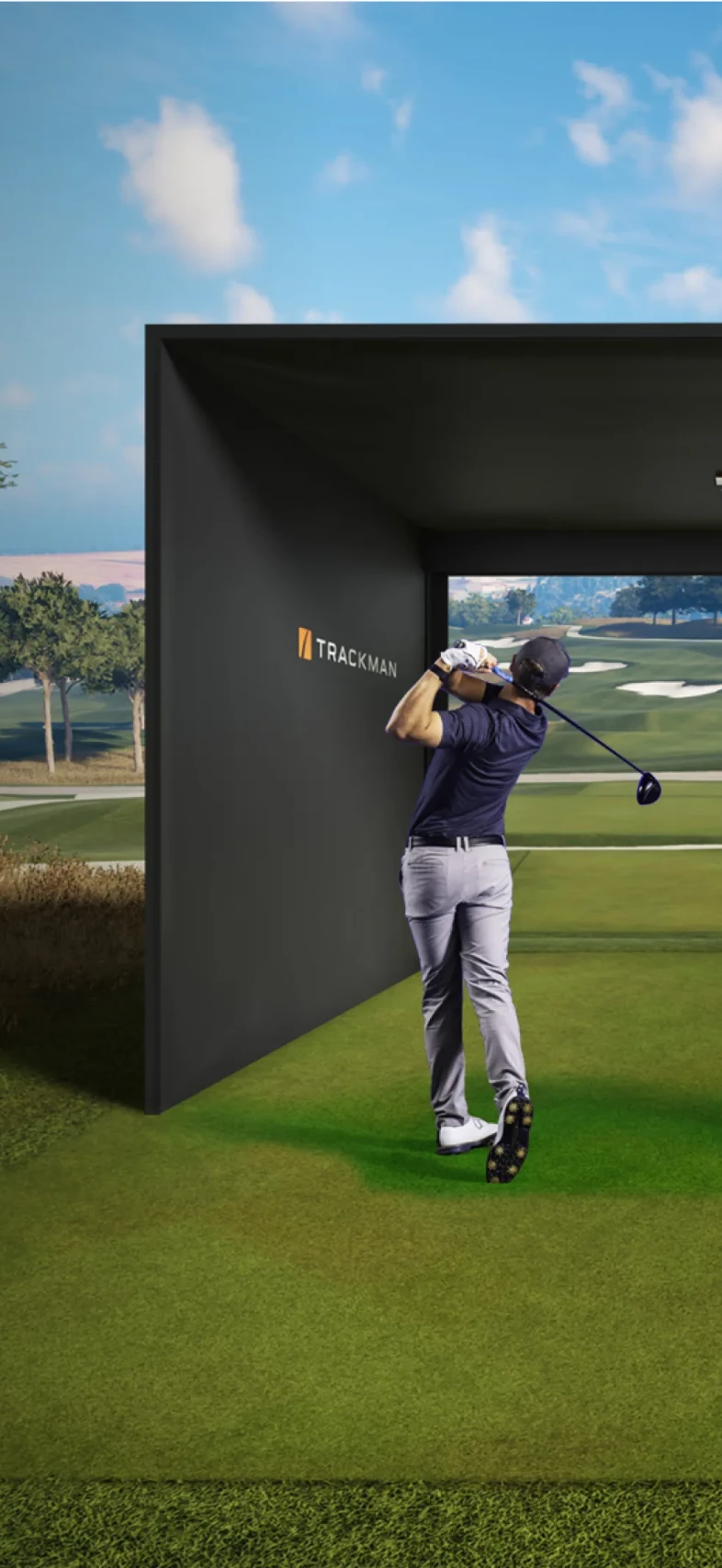 Golfer swings inside a Trackman simulator facing a virtual golf course under a blue sky.